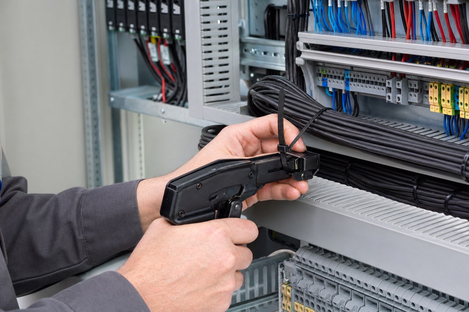 Technician using cable tie tensioning tool inside electrical cabinet to improve installation efficiency