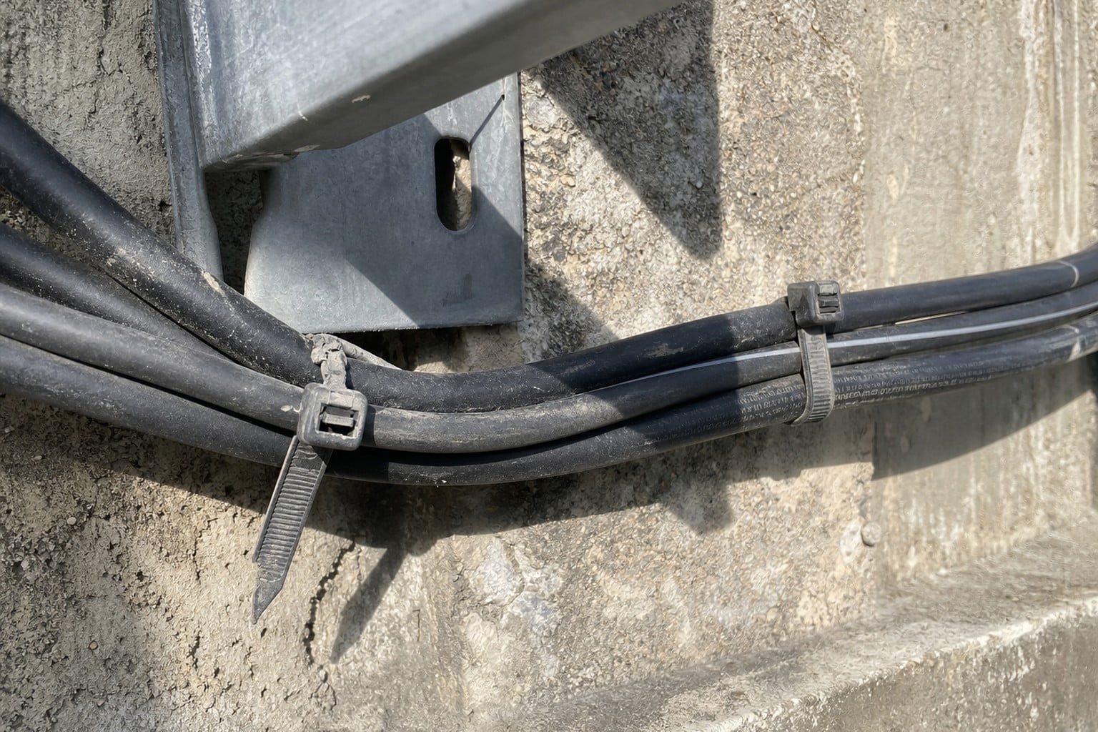 Outdoor cable route with UV-aged loose nylon cable ties and slight cable sag